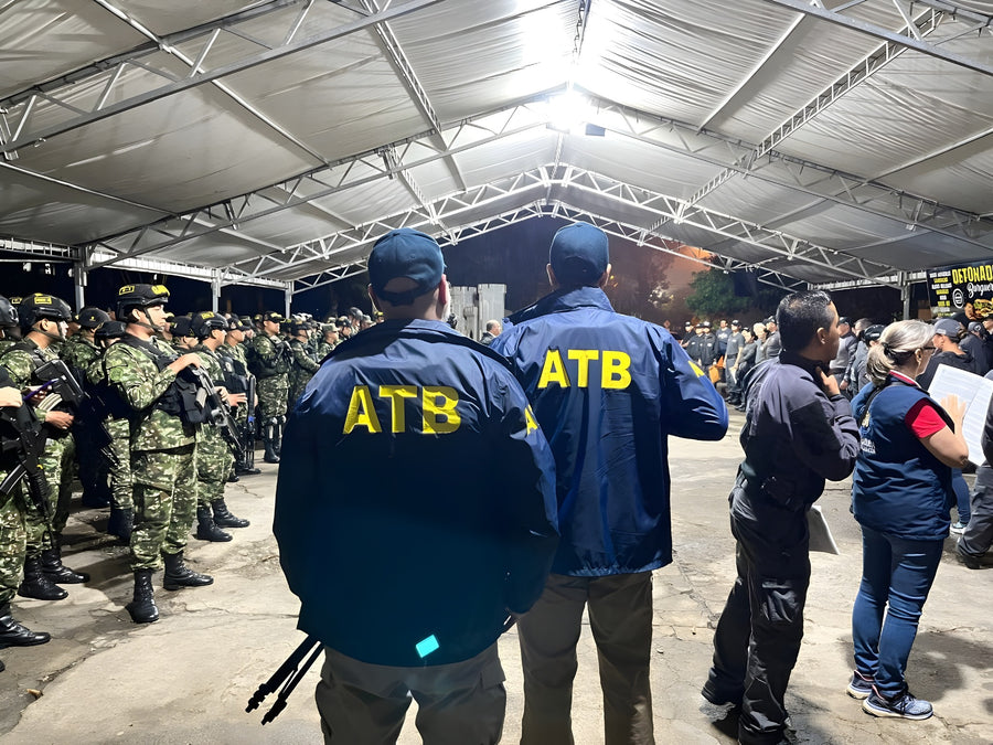 Group of people wearing jackets with 'ATB' on them, standing in a line under a metal roof.