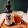 A bottle of Catalyst Cordyceps tincture next to a glass of coffee on a wooden tray, with a green background.