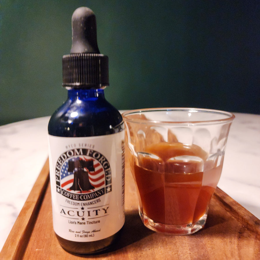 A bottle of Acuity Lion's Mane Tincture placed next to a glass of coffee on a wooden surface, with a green wall in the background.