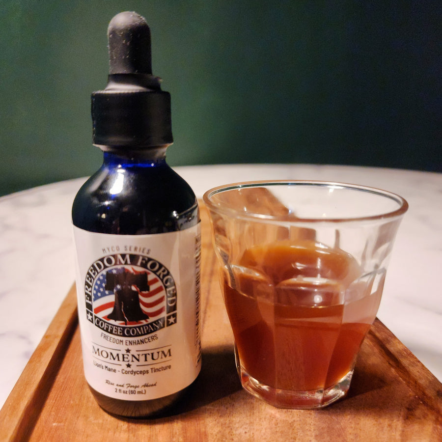 A bottle of Momentum tincture with a dropper, next to a glass of coffee on a wooden tray, against a green background.
